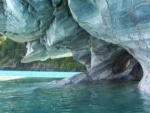 A cave at turquoise water's edge surrounded by white and gray marbled rock