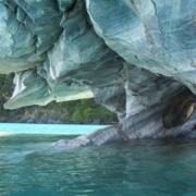 A cave at turquoise water's edge surrounded by white and gray marbled rock