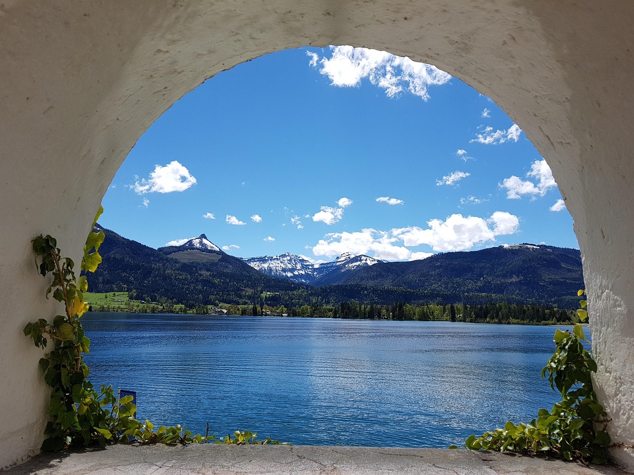 An opening through a cement tunnel to a beautiful and peaceful scene of a lake, green hills and blue sky.