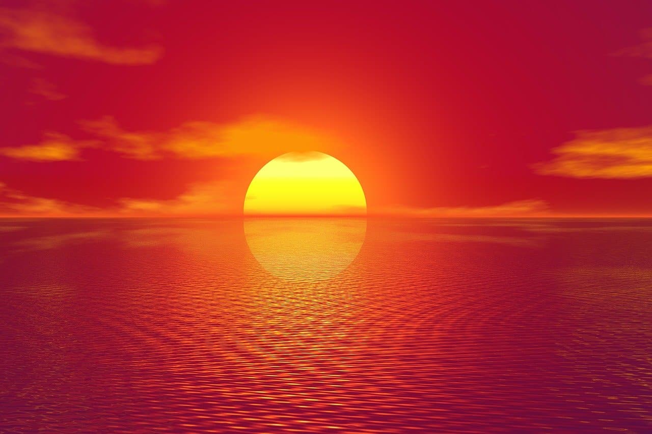 A bright yellow sun setting over water wuith orang hues.