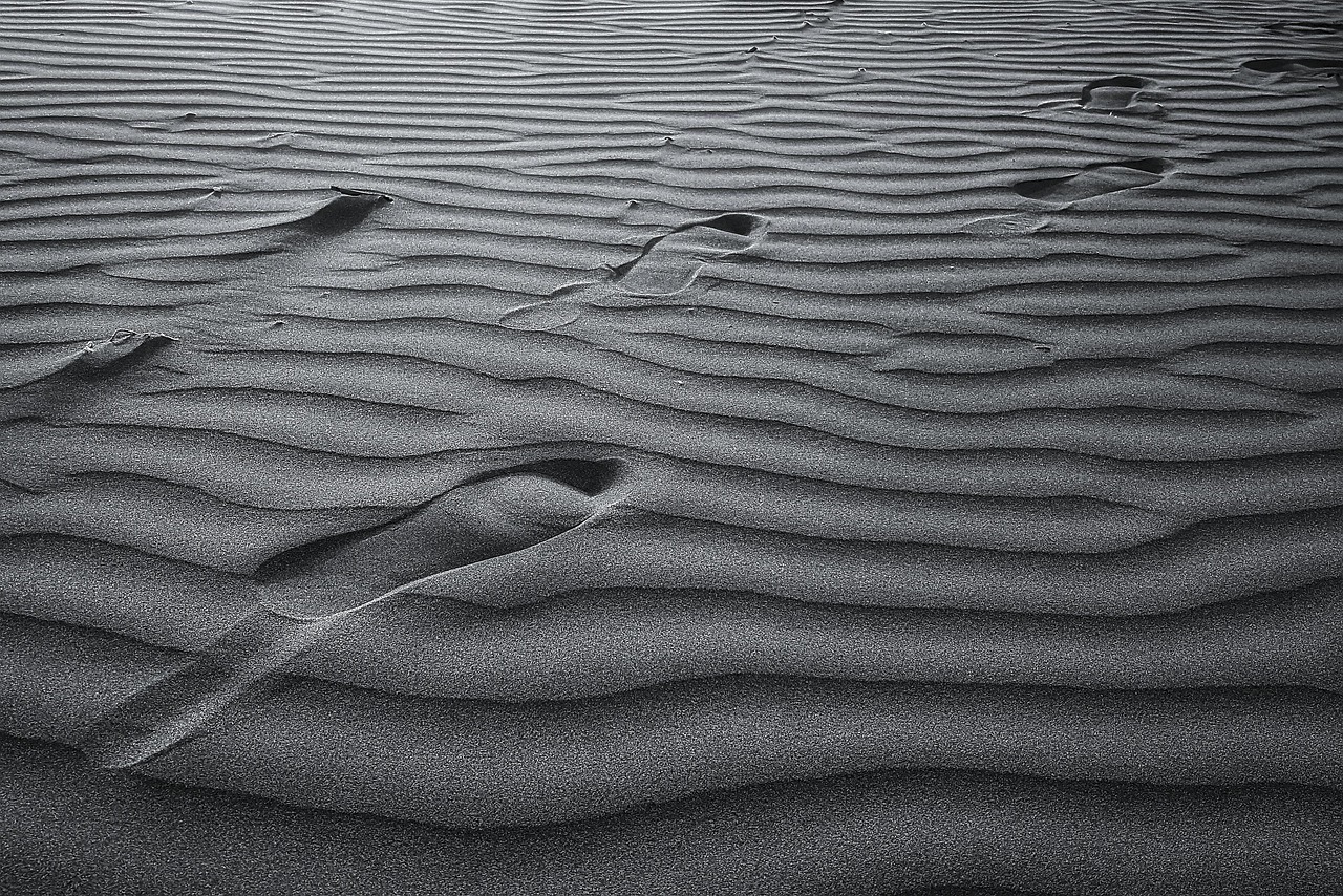 Footsteps in rippling sand in grey tones.