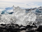 A jagged piece of ice melting on a rock with mountains in the background.