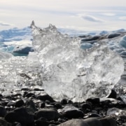 A jagged piece of ice melting on a rock with mountains in the background.
