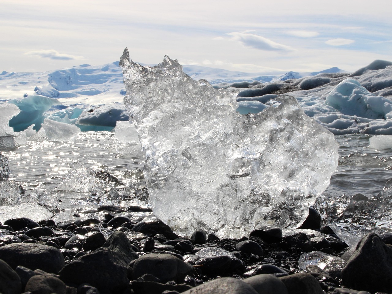 A jagged piece of ice melting on a rock with mountains in the background.