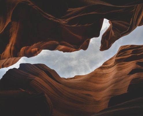 Looking up through an Opening between red rocks to a gray sky