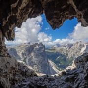 Looking out from inside a cave 's heart shaped opening to mountains, clouds and blue sky.